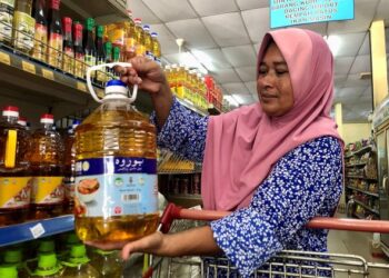 PELANGGAN sebuah pasar mini di Kampung Tualang, Ani Omar, 53, melihat harga pada botol minyak masak dalam sebuah pasar raya di sini hari ini. -UTUSAN/ SHAHIR NOORDIN