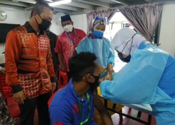 RAZALI Idris (kiri) melihat seorang penggiat pelancongan menerima vaksin Covid-19 di Pengkalan Gawi di Tasik Kenyir, Hulu Terengganu hari ini. - UTUSAN/NOOR HAYATI MAMAT