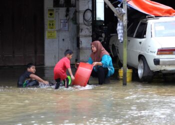 Seorang wanita membasuh peralatan rumahnya sambil ditemani anak-anaknya selepas bengkel kereta miliknya dinaiki air banjir di Kampung Bakong, Pasir Mas semalam. -FOTO/ZULHANIFA SIDEK