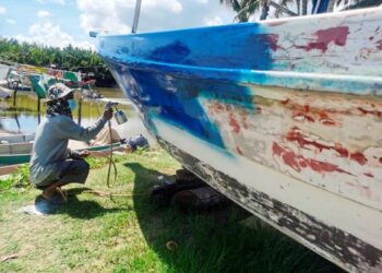 MUSTAKIM Mat Hussin membaiki dan mengecat bot di rumahnya di Pulau Kundor, Kota Bharu kerana tidak dapat ke laut sepanjang musim tengkujuh.– UTUSAN/ ROSALWANI CHE SOH