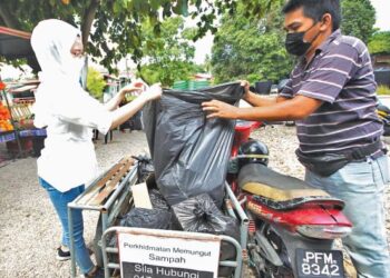 WAN Ahmad Nabil memungut sampah dari rumah pelanggannya di Kampung Kutan Tengah, Tumpat semalam. - UTUSAN/ZULHANIFA SIDEK