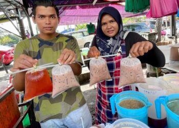 SHAHRIL Ahmad  dan Norfadilah Nordin menunjukkan minuman untuk dijual pada harga RM1 sebungkus di gerai mereka di Pantai Johor, Alor Setar. -UTUSAN/JAMLIAH ABDULLAH