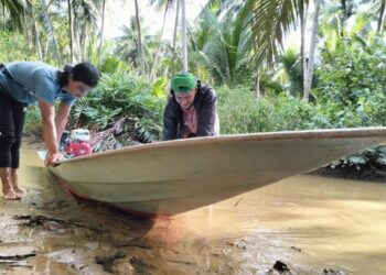 MOHD. Zaki Husin (kiri) bersama rakannya, Azman Abdullah terpaksa menolak bot disebabkan masalah air sungai cetek di Pulau Cendol, Tumpat, Kelantan. – FOTO/ROHANA ISMAIL
