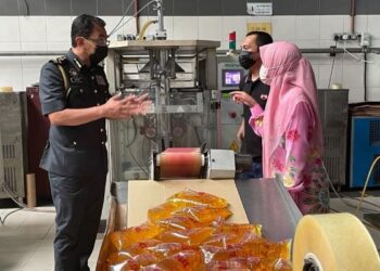 AZMAN Adam (kiri) meneliti bungkusan dan cop dagangan minyak masak bersubsidi di kilang pembungkusan minyak masak Tanjung Pauh Trading di Beris Kubur Besar, Bachok, Kelantan, hari ini. - FOTO/TOREK SULONG