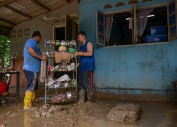 MOHD. Asman Kasman (kanan) dan saudaranya membersihkan rumah yang dipenuhi lumpur akibat banjir di Kampung Teladas di Air Putih, Kemaman hari ini. - UTUSAN/PUQTRA HAIRRY ROSLI