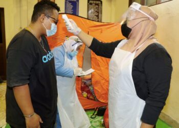 PETUGAS kesihatan memeriksa suhu badan mangsa banjir yang ditempatkan di pusat pemindahan sementara di Jasin, Melaka. - UTUSAN/ RASUL AZLI SAMAD