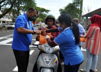 S. DEVA (kiri) mengagihkan barangan segar kepada salah seorang penunggang motosikal di Taman Cendana, Pasir Gudang, semalam. - FOTORAJA JAAFAR ALI