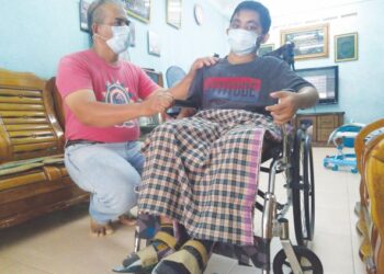MOHD. HUSZAD Mohd. Ali (kiri) melihat keadaan Muhamad Shafiq Ikmal yang lumpuh hampir separuh badan ketika ditemui di kediamannya di Masjid Tanah, Melaka. - UTUSAN/MUHAMMAD SHAHIZAM TAZALI