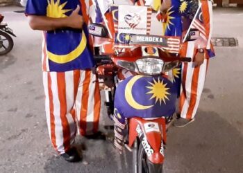 ABDUL RAHMAN Abu Bakar dan Suria Sukirman mengenakan pakaian Jalur Gemilang di samping motosikal dinaiki dihiasi bendera ketika ditemui di Banda Hilir, Melaka. - UTUSAN/AMRAN MULUP