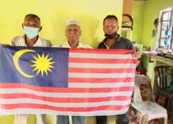 MAT ARIFFIN Mat Deris (tengah) bersama anaknya, Kamaruzaman (kanan) dan Mat Nawi bersemangat memegang Jalur Gemilang di rumah mereka di Kampung Tanjung Buluh, Lipis, Pahang. – UTUSAN/HARIS FADILAH AHMAD