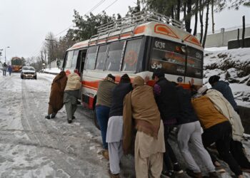 ORANG ramai membantu menolak bas yang terkandas dalam salji di Murree, timur laut Islamabad. - AFP