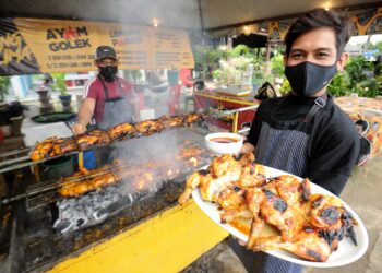 AMIN Izzuddin Sulaiman, 28, menunjukkan set Ayam Golek Panglima beserta kuah kacang sambil kelihatan abangnya, Mohd Nazirul Ikhwan sedang menyiapkan tempahan pelanggan ketika ditemui di Kampung Bagan Pinang Batu 3, Jalan Pantai, Taman Dato Haji Abdul Samad, Port Dickson, semalam. -UTUSAN/MOHD. SHAHJEHAN MAAMIN.
