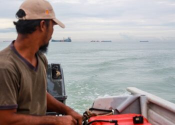 SEORANG nelayan melihat beberapa buah kapal berlabuh di perairan Port Dickson  baru-baru ini.-UTUSAN/MUHAMMAD IZZAT TERMIZIE