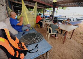 SHAMSUL Kama Khalil memantau anak-anaknya mengulang kaji pelajaran sambil dia membaiki jaring ikan di Port Dickson, semalam. - UTUSAN/MOHD. SHAHJEHAN MAAMIN