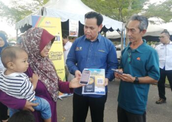 SAHARUDDIN Mohd. Kia (tengah) membantu pengunjung mengimbas kod QR untuk mendapatkan insentif kewangan dalam bentuk e-dompet pada majlis pelancaran Bazar Ramadan Rahmah Negeri Terengganu 2023 di Binjai Rendah, Marang, Terengganu, petang semalam. - UTUSAN/NOOR HAYATI MAMAT