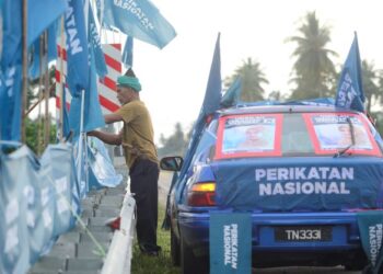 SEORANG penyokong memperbetulkan kedudukan bendera yang tumbang dan ditiup angin di jalan menuju Tanjung Gemok, Rompin, Pahang. -UTUSAN/SHAIKH AHMAD RAZIF