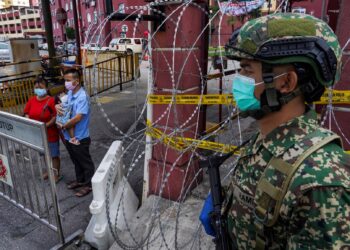 Seorang anggota tentera memerhatikan pasangan warga Myanmar yang sedang mendukung anak mereka yang demam di pintu masuk  Pangsapuri Mentari Court yang dikenakan Perintah Kawalan Pergerakan Diperketatkan (PKPD) bermula semalam hingga 14 Julai 2021. - UTUSAN/MUHAMAD IQBAL ROSLI