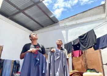 YUSOF Md. Nor bersama anaknya, Mohd. Syamin Azhar memegang baju raya sambil melihat bumbung rumah mereka di Kampung Tok Pulau, Arau, Perlis yang diterbangkan angin kencang kelmarin. – UTUSAN/NAZLINA NADZARI