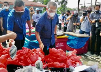 MUHYIDDIN Yassin (dua kiri) melihat makanan basah yang akan disampaikan kepada keluarga-keluarga yang sedang dikuarintin ketika majlis penyampaian di Kompleks Penghulu Mukim Sungai Raya, Bukit Pasir di Muar, Johor. -UTUSAN/NUR ALINA HASSAN