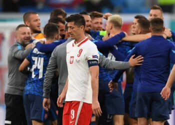 BINTANG penyerang Poland, Robert Lewandowski melangkah lemah melewati pemain Slovakia yang meraikan kemenangan mereka dalam aksi Kumpulan E di Stadium Saint Petersburg, Rusia hari ini. - AFP
