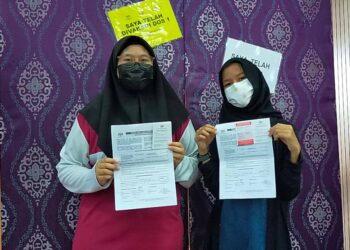 EMI KHADIJAH (kiri) dan adiknya, Emi Fitriah menunjukkan borang persetujuan menerima vaksin Covid-19 di PPV PICK Remaja di SMK Proton City di Tanjung Malim, Perak, hari ini. - UTUSAN/ASLIZA MUSA