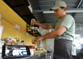 Peniaga, Ahmad Muzakkir Ahmad Zabri 30, mengikuti siaran langsung pembentangan Belanjawan 2023 oleh Perdana Menteri melalui telefon pintarnya di kedai makannya di Sungai Rokam,  Ipoh. semalam.  - UTUSAN/MUHAMAD NAZREEN SYAH MUSTHAFA