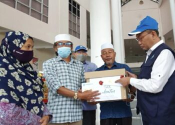 AWANG Hashim menyerahkan cek dan bakul prihatin Perkeso kepada Ibrahim Majid (dua dari kiri) sambil diperhatikan isterinya, Norhayati Saad di Jeti Pelancongan Pekan Rabu, Kuah, Langkawi. - UTUSAN/NUR AMALINA AZMAN