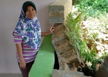 WARDIANI Ayu Baba menunjukkan benteng yang roboh dan menghempap dinding rumahnya di Solok Hasan Yasin, Pantai Rombang, Melaka. – UTUSAN/AMRAN MULUP