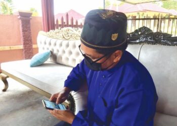 MOHD. Rizaini Ghazali melihat gambar Allahyarham  Muhammad Adham Hazim ketika ditemui di rumahnya di Kampung Tepoh di Kuala Nerus, semalam. – UTUSAN/TENGKU DANISH BAHRI TENGKU YUSOFF