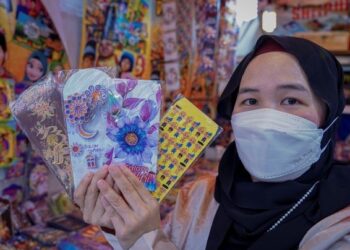 PENIAGA, Nurul Farhana Abdul Shukur, 35 menunjukkan sampul duit raya yang dijual dengan pelbagai corak pilihan dengan harga RM3 hingga RM4 untuk satu pek ketika tinjauan di Bazar Aidilfitri Jalan Tunku Abdul Rahman (Jalan TAR).  - UTUSAN/FARIZ RUSADIO