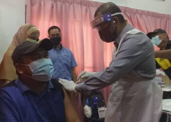 NOOR Azmi Ghazali (kanan) memberikan suntikan vaksin Covid-19 kepada seorang guru SMK Alor Pongsu, Mohd. Fauzi Ramli di Dewan SMK Abu Bakar Al-Baqir, Bagan Serai hari ini. - UTUSAN/WAT KAMAL ABAS