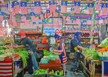 NIK Mohd. Fariz Nik Sabri, 10, (tengah) lengkap berpakaian seragam Jalur Gemilang membantu keluarganya berniaga di Pasar Chabang Tiga, Terengganu, yang turut dihiasi 10,000 bendera itu. - UTUSAN/PUQTRA HAIRRY ROSLI