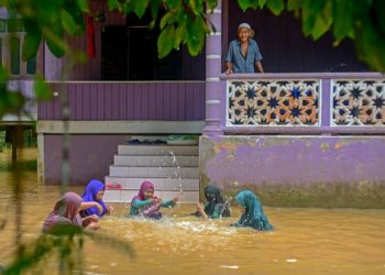 MOHD. Matnor Abu Bakar melayani cucu-cucunya bermain banjir di hadapan rumah mereka di Kampung Bukit Tadok, Hulu Terengganu, semalam. - UTUSAN/PUQTRA HAIRRY ROSLI