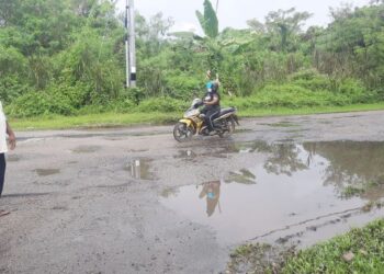 K.Murthy (kiri) menunjukkan jalan berlubang yang mengundang kebimbangan pengguna di Jalan Damai 3 yang terletak di simpang masuk ke Taman Damai, Padang Serai di Kulim. -UTUSAN/AZAHAR HASHIM