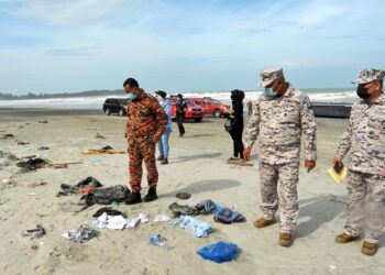 Anggota Maritim Malaysia dan bomba melihat pakaian milik pendatang asing yang bersepah selepas bot dinaiki mereka karam di Pantai Tanjung Balau, Kota Tinggi semalam. -UTUSAN/RAJA JAAFAR ALI