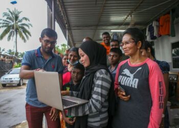 V.Barathidhasa (kir) membantu Siti Nor Dalilawati Syahril (bertudung) mendapatkan akses internet di Kampung Ladang UP, Bukit Selambau, semalam. -FOTO: SHAHIR NOORDIN