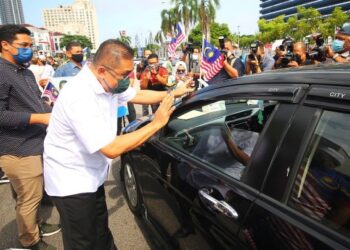 TAKIYUDDIN Hassan memasang Jalur Gemilang pada kereta orang ramai di depan Pusat Khidmat Ahli Parlimen Kota Bharu hari ini. - UTUSAN/ZULHANIFA SIDEK