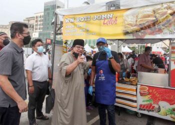 TENGKU Adnan Tengku Mansor menyerahkan apron dan topi kepada para peniaga bazar Ramadan di Presint 3, Putrajaya. - FOTO/FAISOL MUSTAFA