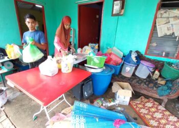 AHSANUL HUSNA Maizir dibantu anaknya mengemas barang-barang yang dapat diselamatkan akibat banjir kilat melanda Kampung Tengah, Pulau Gadong, Melaka. - UTUSAN/AMRAN MULUP