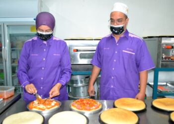 MOHD. Hafiz Ahmad dan isterinya, Nurhayati Ismail (kiri) ketika menyediakan piza jualan mereka di kedai Pizza Ukhwah, pekan Pantai, Seremban.-UTUSAN/ZAKKINA WATI AHMAD TARMIZI.