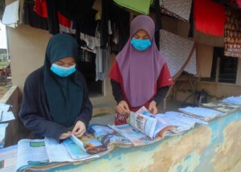 NUR Marsya Farzana Samtidar dan adiknya, Nur Qistina Izzati (kiri) menjemur buku teks yang terendam air akibat banjir di Kampung Cemperai, Dengkil, Selangor, baru-baru ini. - UTUSAN/FAISOL MUSTAFA