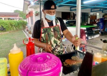 WAN Kharizal Wan Azmin menyediakan burger buat pelanggan di hadapan rumahnya di Taman Intan, Arau, Perlis. - UTUSAN/MOHD. HAFIZ ABD. MUTALIB
