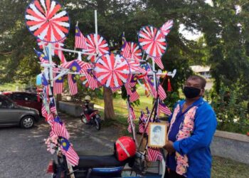 M. Gunaselan menunjukkan gambar mendiang bapanya yang dibawa bersama motosikal miliknya yang telah dihias dengan Jalur Gemilang ketika ditemui di Taman Rekreasi Tampin, Tampin semalam.-UTUSAN/NOR AINNA HAMZAH
