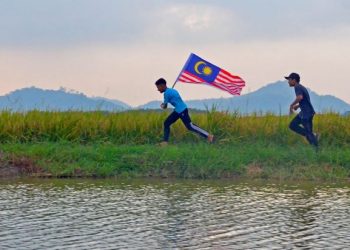 Muhamad Syamirul Munafis (kiri) bersama rakannya, Muhamad Zarul Hairi Edysham berlari sambil membawa Jalur Gemilang sempena sambutan Hari Kebangsaan di Kampung Permatang Langsat, Kepala Batas, Pulau Pinang, baru-baru ini. – UTUSAN/AMIR IRSYAD OMAR