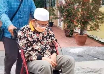KEADAAN Mohd. Kazim Elias yang dibantu ketika menggunakan kerusi roda untuk bergerak berikutan sakit kaki kiri yang beliau alami sejak dua minggu lalu. - UTUSAN/MEDIA SOSIAL
