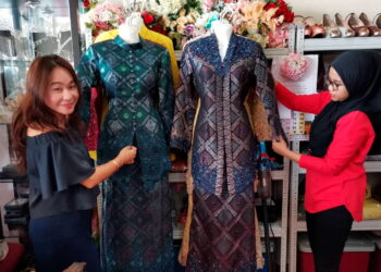 LIM Ai Lee (kiri) yang dibantu pekerjanya melihat pakaian pengantin di butiknya di Hutan Melintang ketika ditemui di Bagan Datuk baru-baru ini. - UTUSAN/AIN SAFRE BIDIN