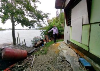SEORANG penduduk menunjukkan jarak rumahnya yang terlalu dekat dengan Sungai Kurau akibat hakisan tebing di RPT Kampung Raja Bashah, Kuala Kurau dekat Parit Buntar. – UTUSAN/WAT KAMAL ABAS