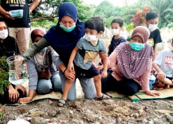 SAMBIL memegang Adeeb Hud, Shamshira Mohamad Norizin menyiram air mawar ketika menziarahi kubur suami dan dua anaknya di Kampung Chenderong Balai, Teluk Intan baru-baru ini. – Utusan/AIN SAFRE BIDIN