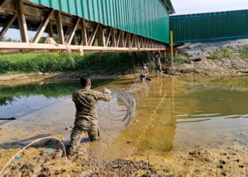 Anggota tentera dari  Batalion Kedua Rejimen Renjer Diraja, Kem Syed Putra, Ipoh meredah selut ketika memasang kawat duri  merentangi anak Sungai Bidor di  sekitar kawasan asrama, kilang dan tapak binaan Central Medicare di Teluk Intan, semalam. - UTUSAN/AIN SAFRE BIDIN