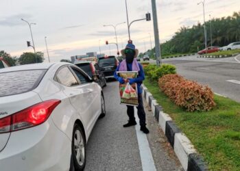 PENJAJA menjual jeruk mangga kepada  pengguna kenderaan yang berhenti sebuah persimpangan lampu isyarat di Teluk Intan. - UTUSAN/AIN SAFRE BIDIN